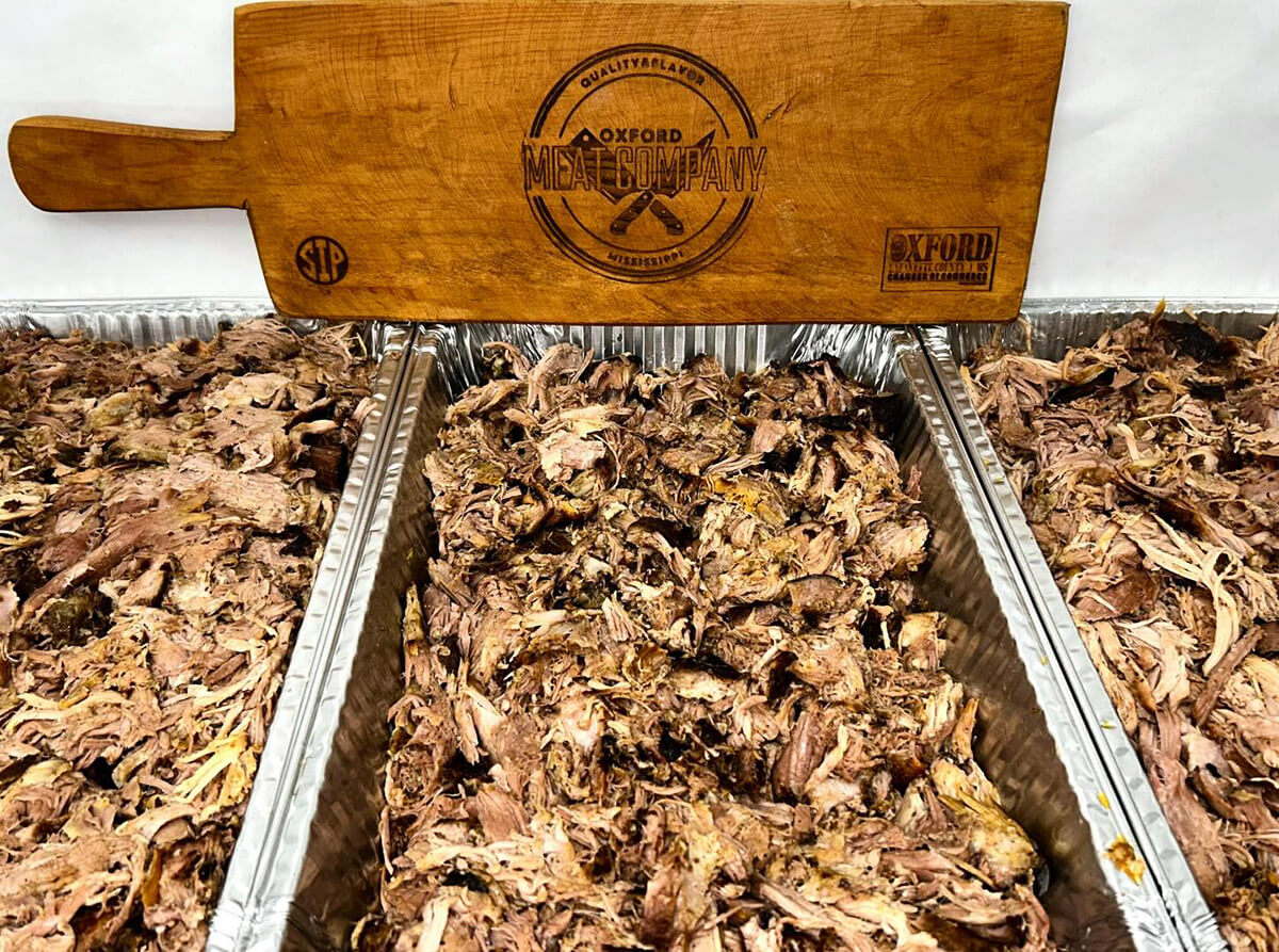Tray of slow-cooked pulled pork next to an Oxford Meat Company branded board